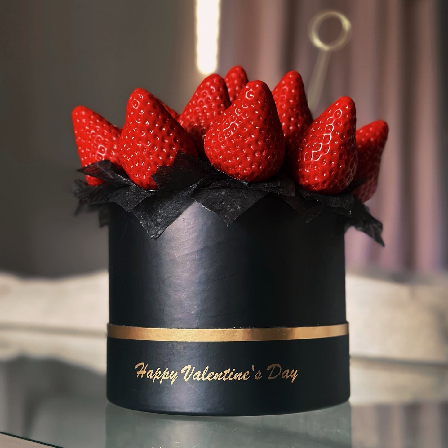 Black box with red strawberries arranged like flowers on a reflective surface.
