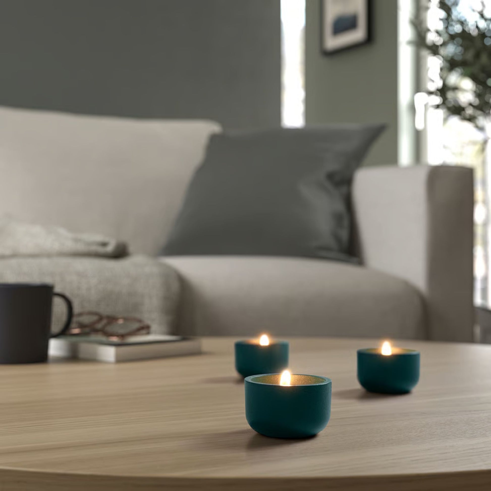 deep turquoise tealight candle holder on a wooden table with a blurred sofa and window in the background