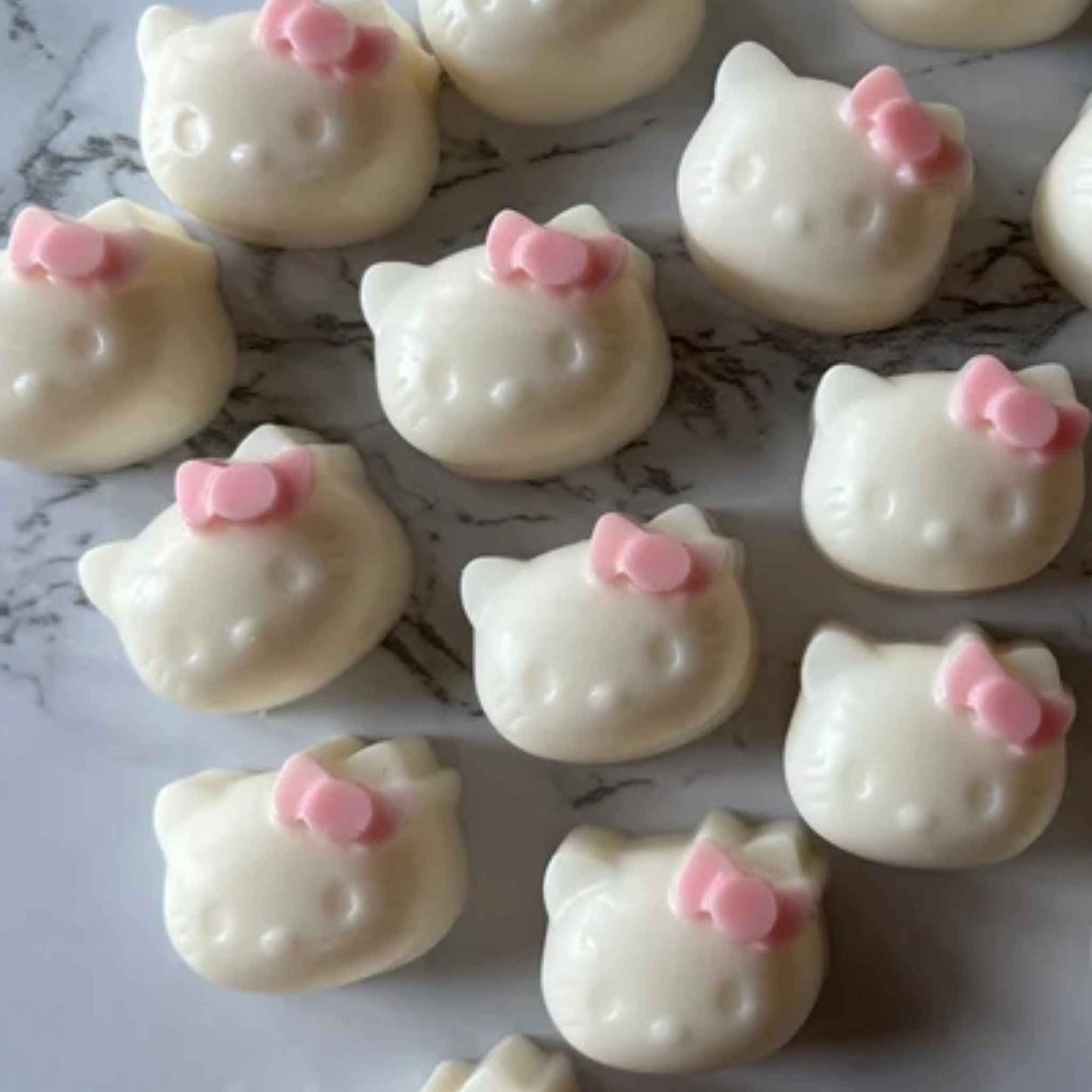 White cat-shaped wax melts with pink bows on a marble surface
