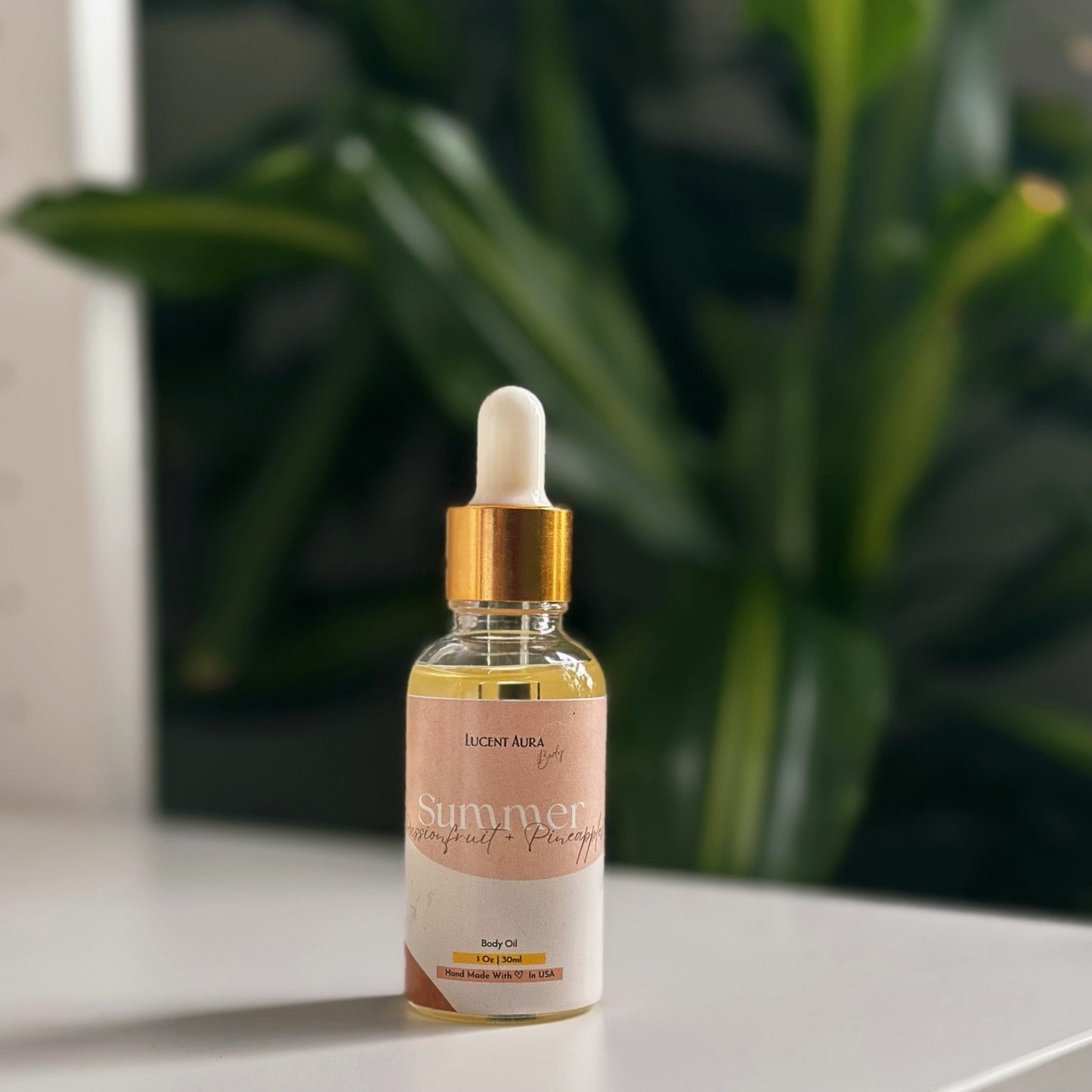 Bottle of Lucent Aura body oil on a white surface with a blurred green plant in the background