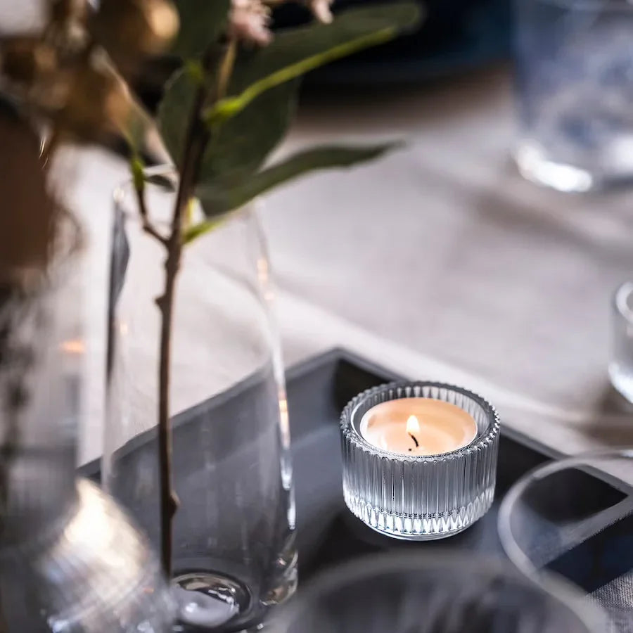 Ribbed glass tea-light holder and a lit candle with a blurred background