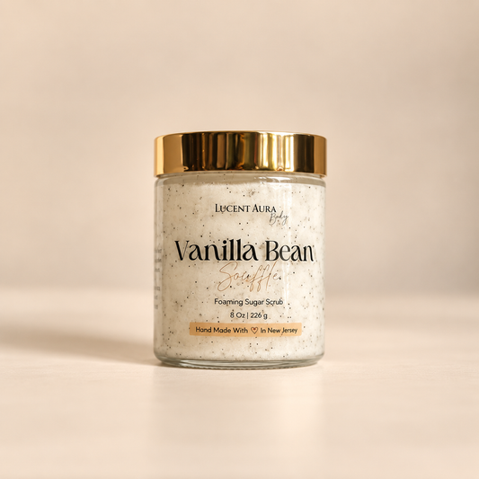 A jar of Lucent Aura Body Vanilla Bean Scuffie Foaming Sugar Scrub with a gold metallic lid, set against a warm beige background.