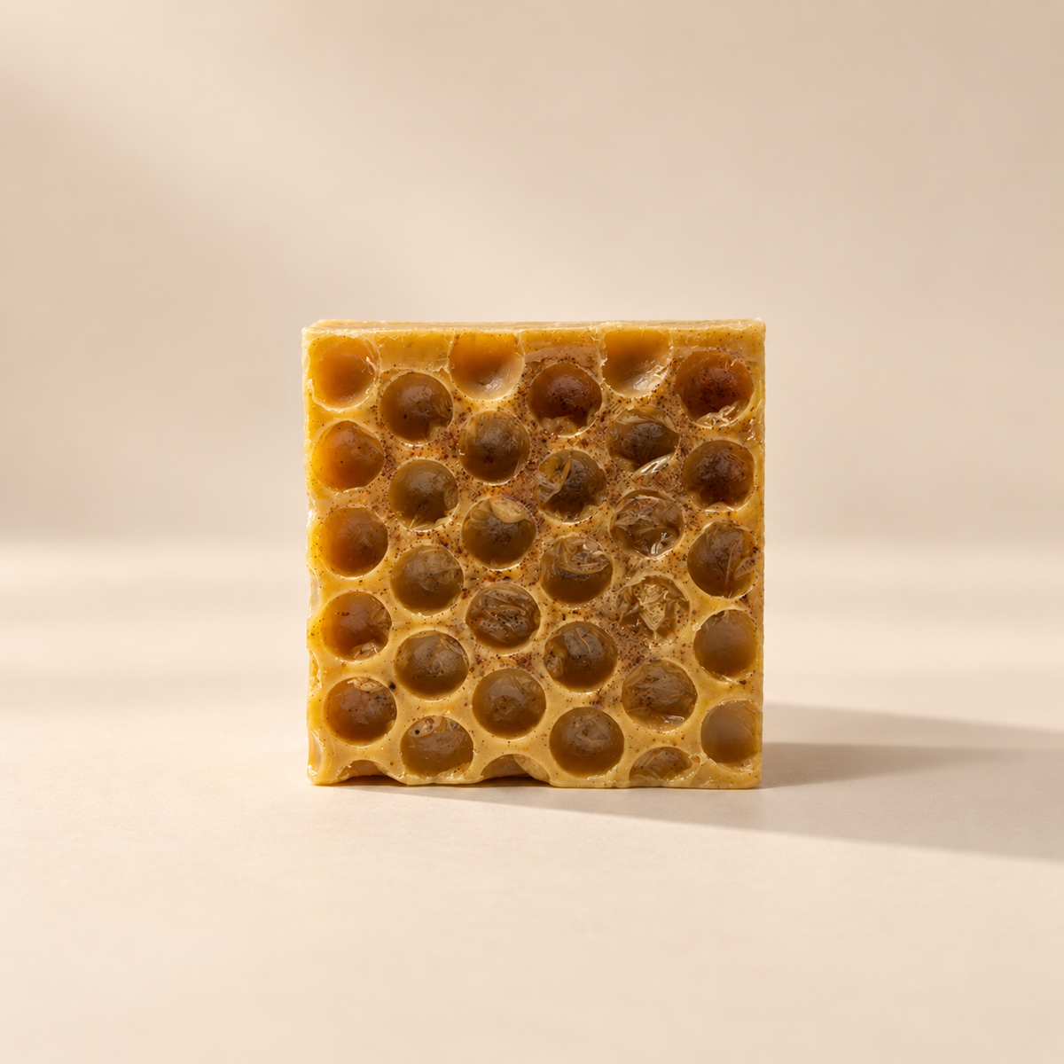 A square bar of honeycomb te=urmeric and Honey soap standing upright on a warm beige background. The soap features a natural golden-yellow outer structure with dark amber honey-filled hexagonal cells visible throughout.