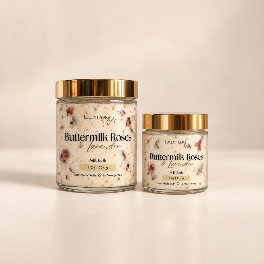 Two glass jars of Lucent Aura Buttermilk Roses & Lavender Milk Bath with gold lids, one 8 oz and one 4 oz, on a warm beige background.