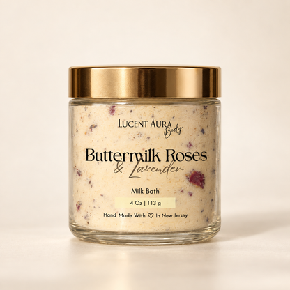 A glass jar of Lucent Aura Buttermilk Roses & Lavender Milk Bath with a gold metallic lid, set against a clean, warm off-white background.