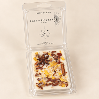 A clear plastic clamshell package containing a white wax melt or wax melt tin with visible botanical and spice inclusions, shown open on a plain light beige background. The inside lid has printed branding and design text.