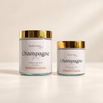 Two glass jars of Lucent Aura Champagne Toast Foaming Sugar Scrub with gold lids, one larger and one smaller, on a clean white background.