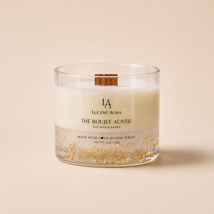 A Lucent Aura soy wax candle in a clear glass jar with a wooden wick, featuring a white wax body, a gold glitter bottom layer, and a small wooden slice insert on the lid, set against a solid beige background.