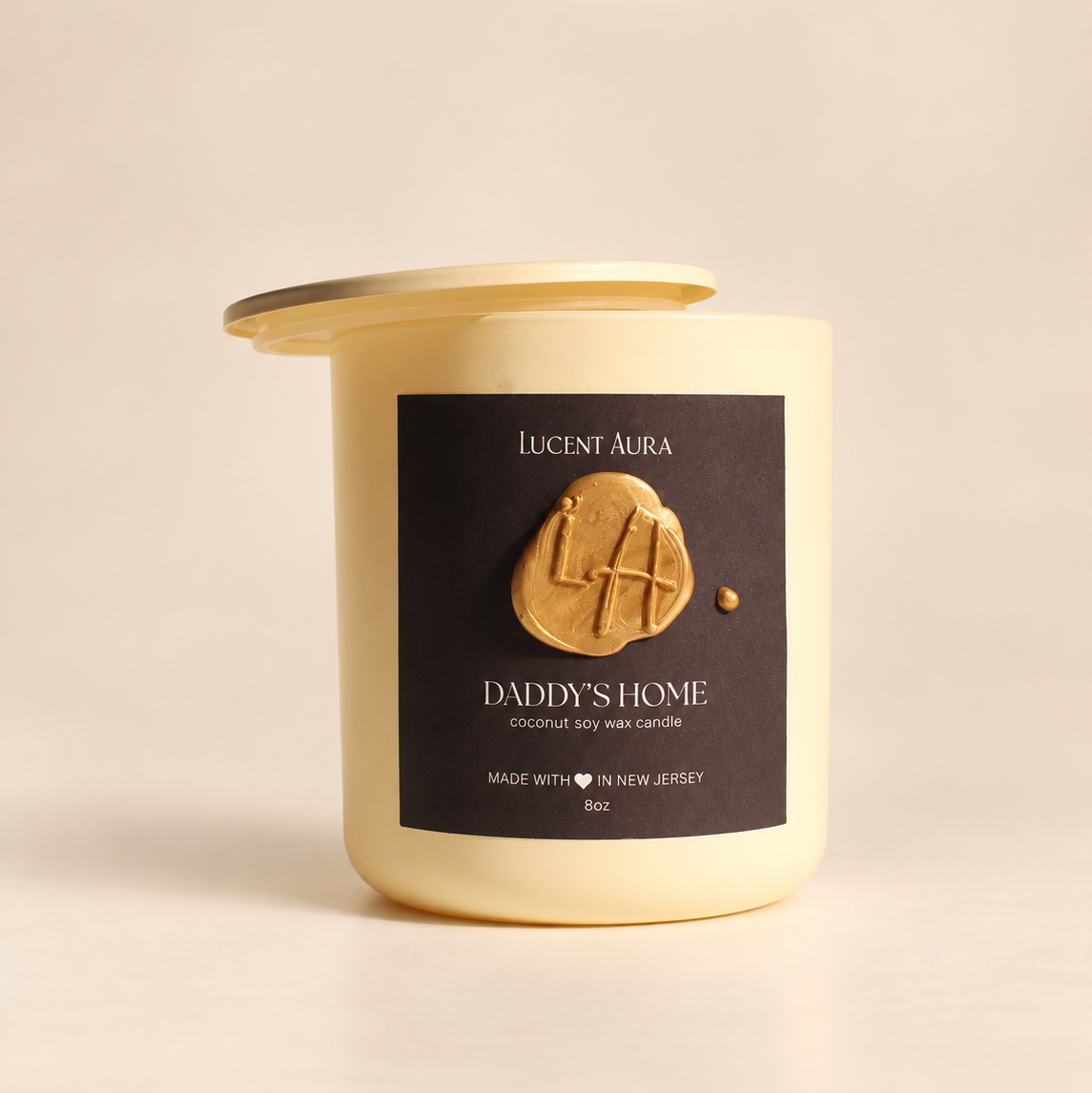A cream-colored candle jar with a gold-toned lid and a dark brown label reading 'Lucent Aura' and 'Daddy's Home', photographed on a warm beige background.