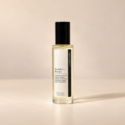A clear glass bottle of room spray with a black cap and a white label reading 'Daddy's Home' and 'LUCENT AURA', filled with pale yellow liquid, set against a warm beige background.
