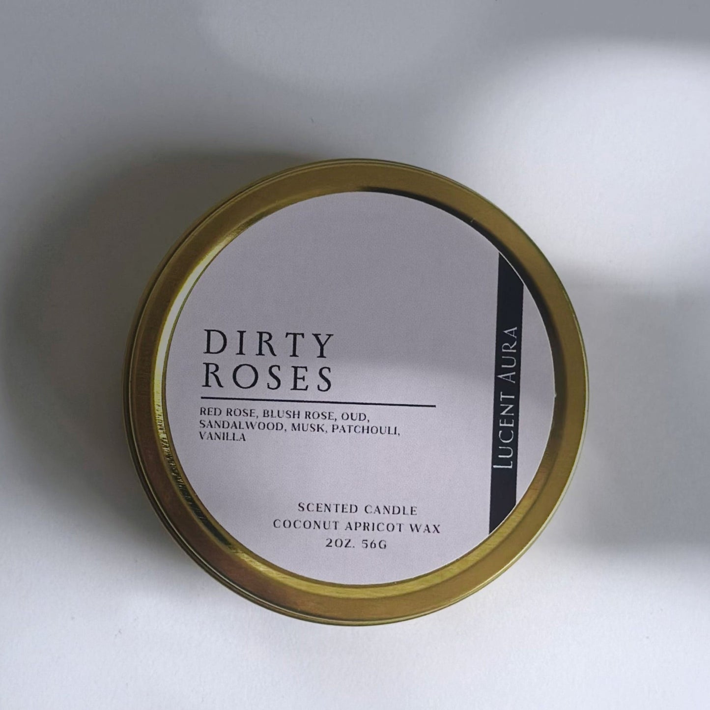 Candle tin labeled 'Dirty Roses' on a white background in a gold tin with soft shadows.