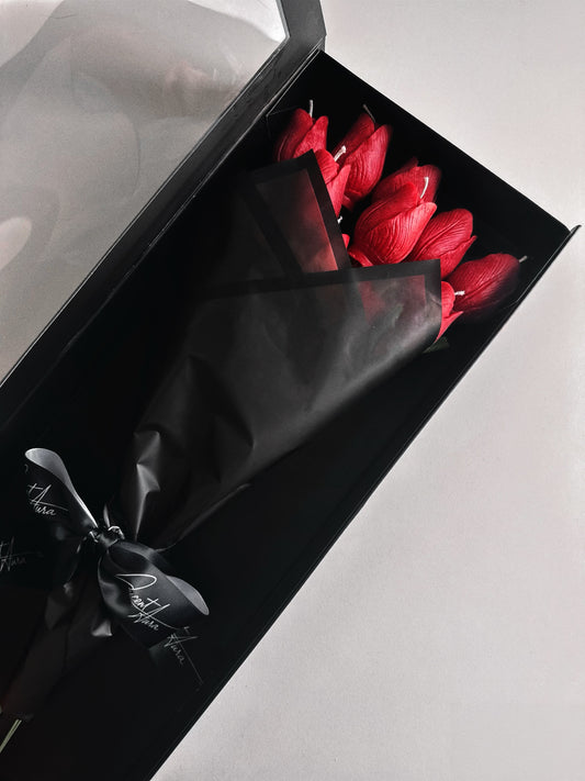 Red tulip candle in a black box with a black ribbon on a light gray background