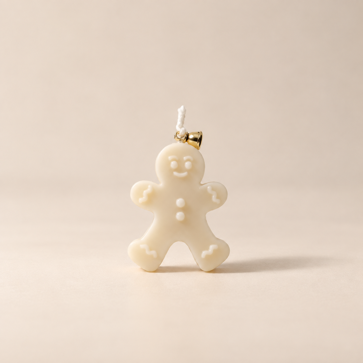 An off-white gingerbread man candle with a small gold-tone bell at the top, shown on a plain beige background.