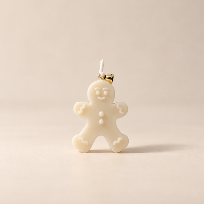 An off-white gingerbread man candle with a small gold-tone bell at the top, shown on a plain beige background.