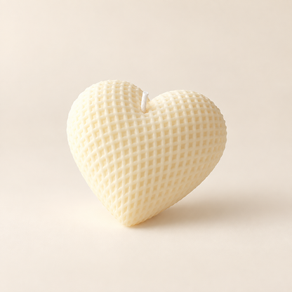 A heart-shaped wax candle with a textured honeycomb pattern, shown on a warm cream background.