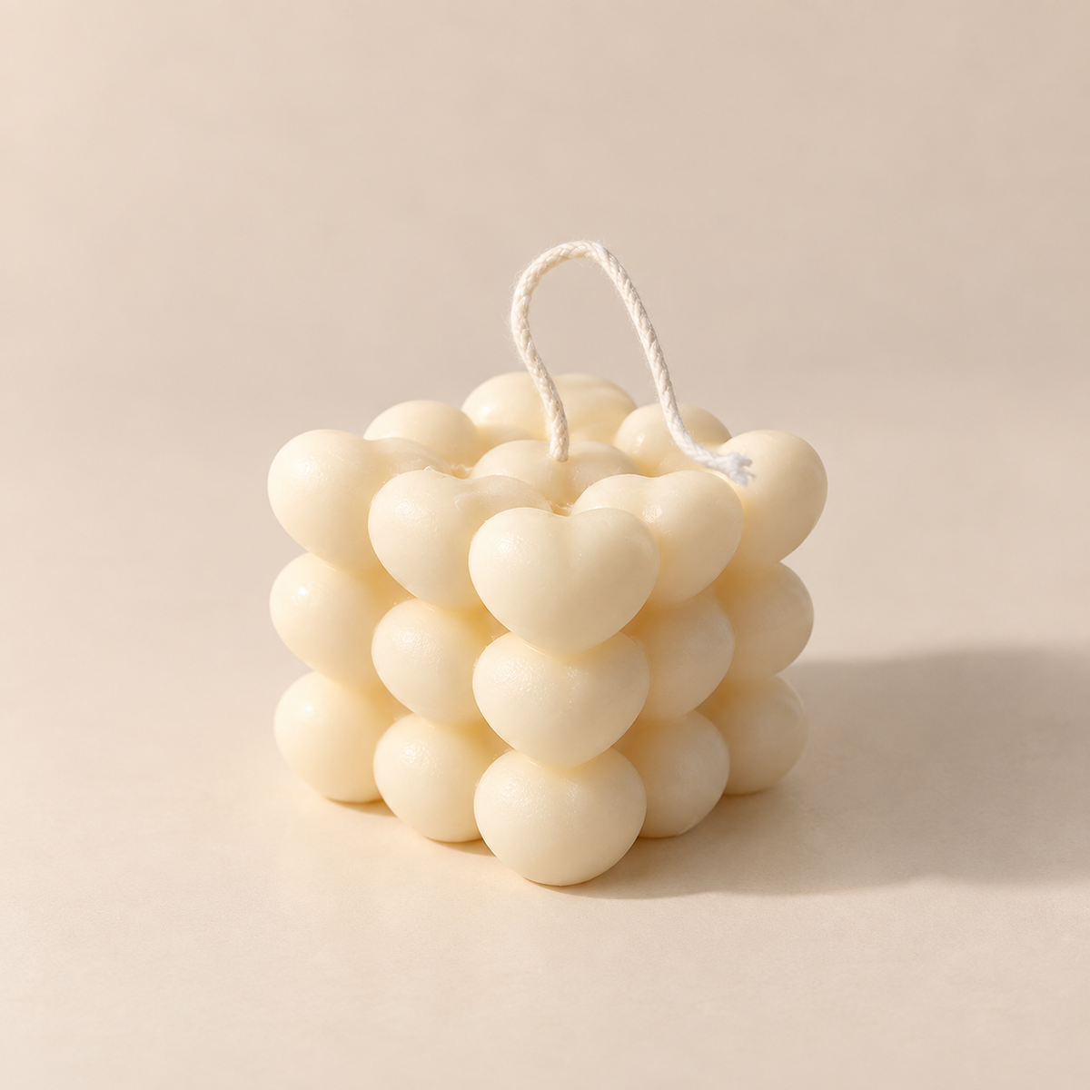 An off-white bubble candle made of heart-shaped wax clusters with a white cotton wick, set against a solid beige background.