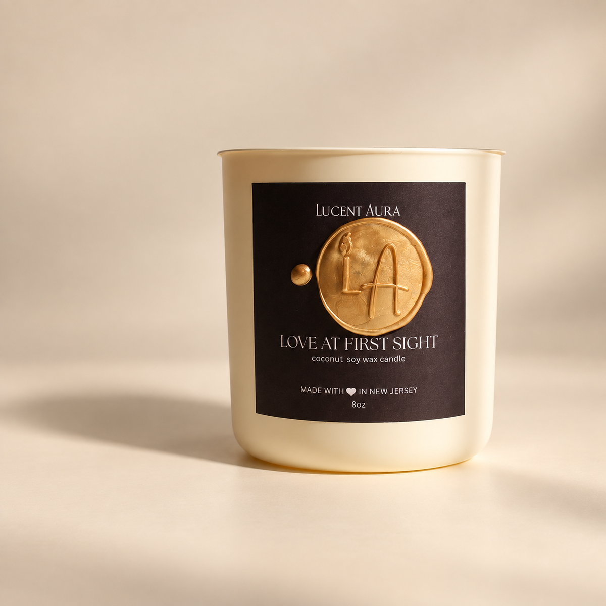 A Lucent Aura soy wax candle in a cream-colored glass jar with a black label featuring a gold wax seal design. The candle is photographed on a warm beige background with soft, directional shadows.