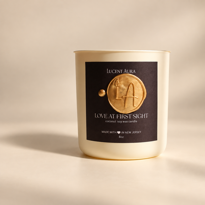 A Lucent Aura soy wax candle in a cream-colored glass jar with a black label featuring a gold wax seal design. The candle is photographed on a warm beige background with soft, directional shadows.