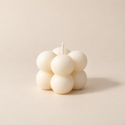 A mini bubble candle made of seven matte off-white spheres with a single wick, photographed on a warm beige studio background.