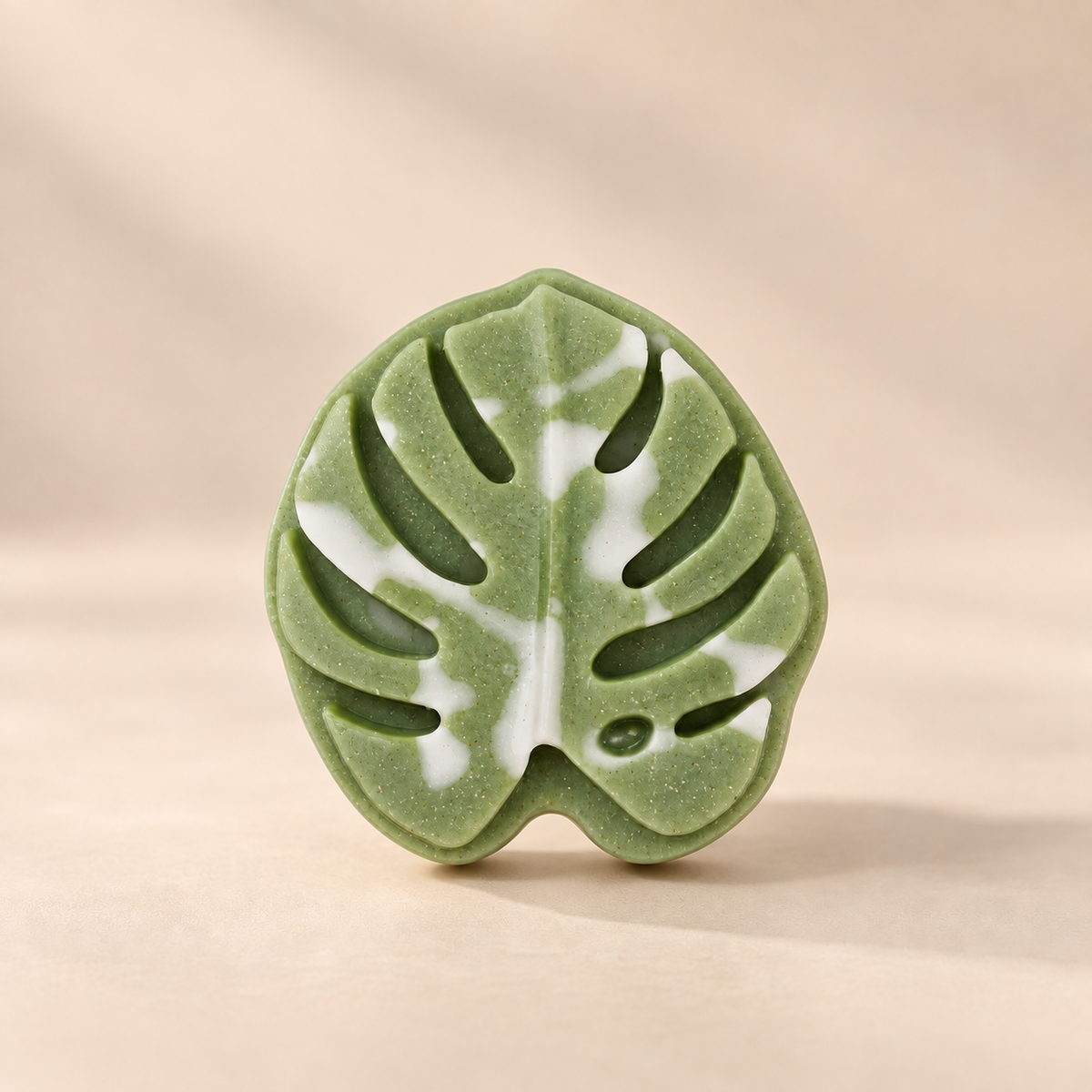A green and white marbled monstera leaf-shaped ring on a warm beige background.