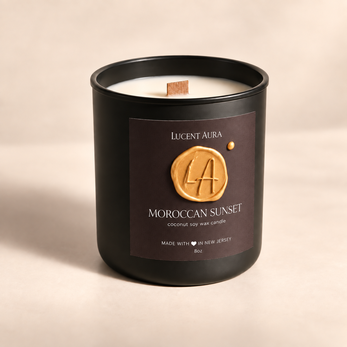 A Lucent Aura 'Moroccan Sunset' coconut soy wax candle in a matte black glass jar with a dark brown label featuring a gold wax seal design, set against a warm beige background.