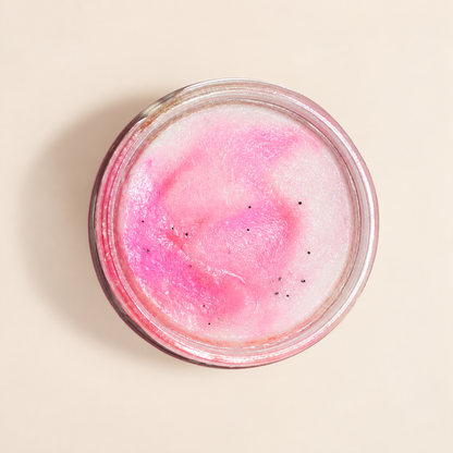 A top-down view of a clear glass jar containing a pink and white marbled sugar scrub, with tiny black specks, set against a solid beige background.