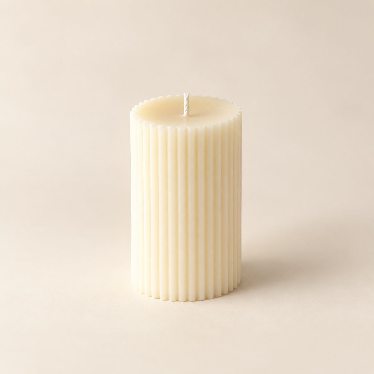 A single cream-colored ribbed pillar candle with a white wick, standing upright against a solid, warm beige background.