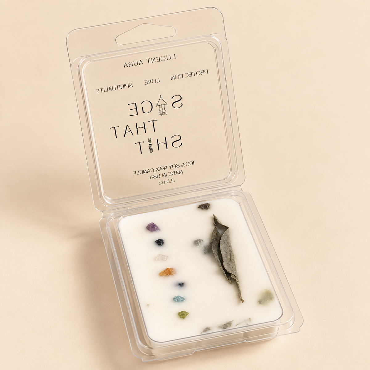 An open clear plastic wax melt clamshell package on a warm beige background. The white wax insert contains embedded stones and a dried leaf, with the brand name 'LUCENTIA AURA' and scent name 'SAGE THAT SHIT' printed on the inside of the lid.