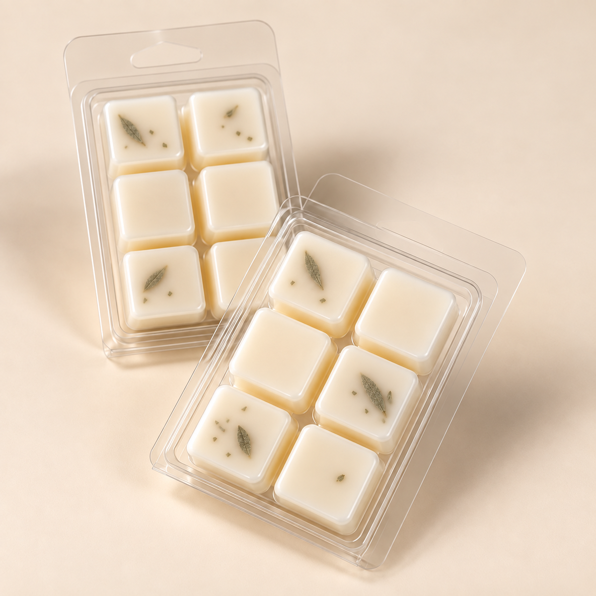 Two clear plastic packages containing eight square cream-colored wax melts, each with a small dried botanical inlay, set against a warm beige background.