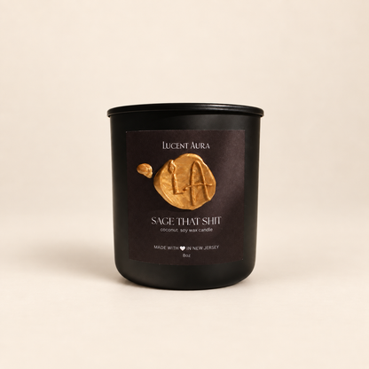 A matte black soy wax candle jar by Lucent Aura with a dark brown label featuring a gold wax seal logo and the scent name 'Sage That Shit'.