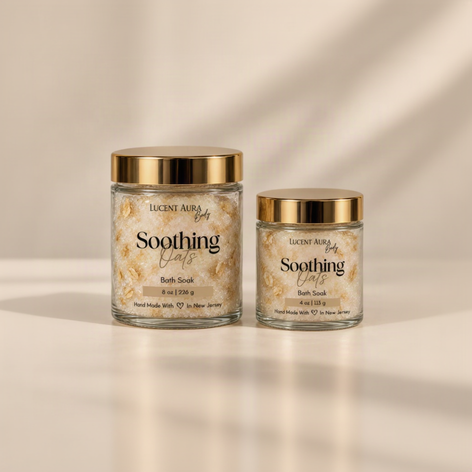 Two glass jars of Lucent Aura Soothing Oats Bath Soak with gold lids, one 8 oz and one 4 oz, on a warm beige background.