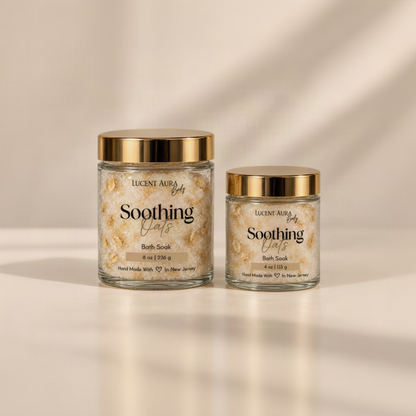 Two glass jars of Lucent Aura Soothing Oats Bath Soak with gold lids, one 8 oz and one 4 oz, on a warm beige background.