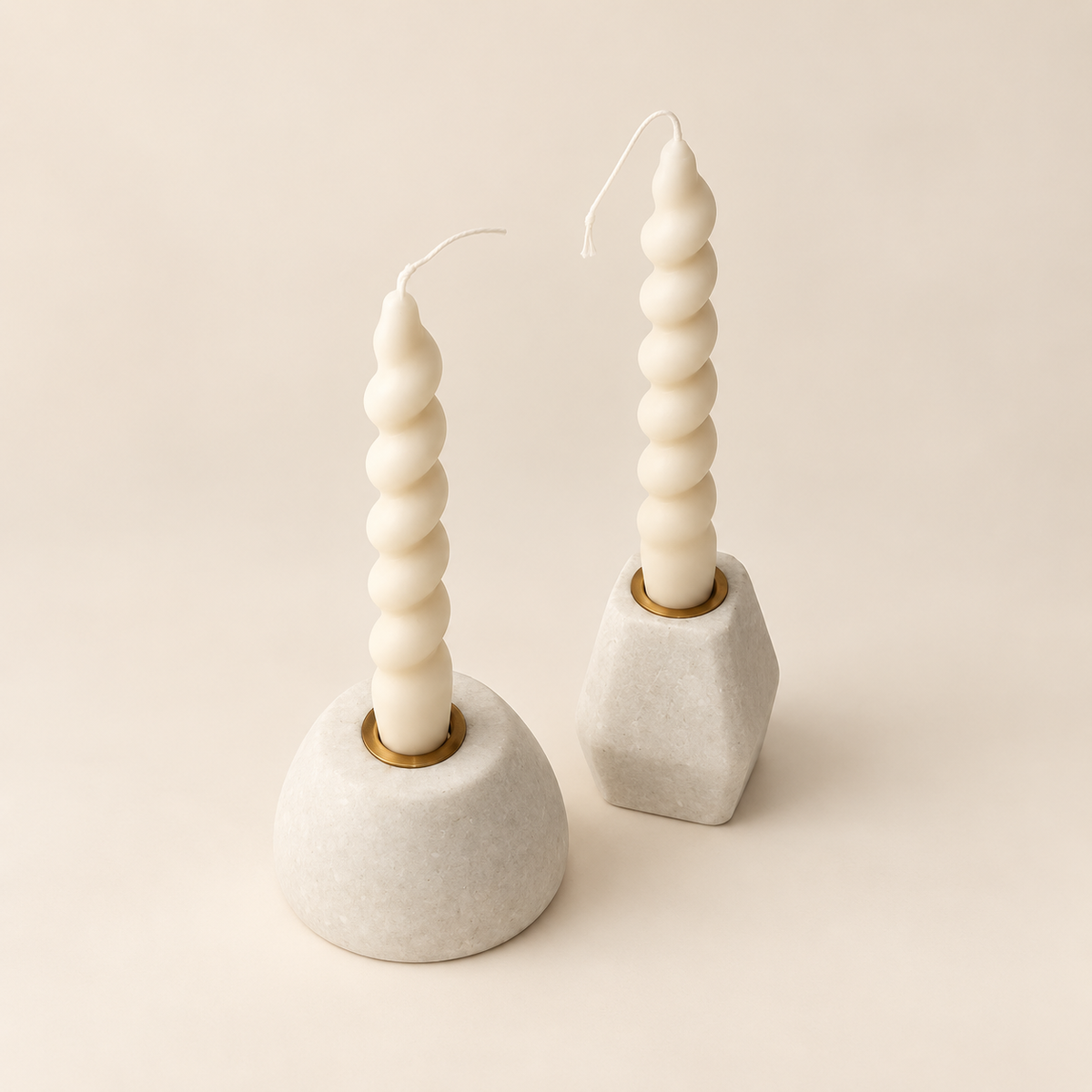 Two sculptural spiral taper candles in matte off-white, displayed in modern geometric holders on a warm beige background.