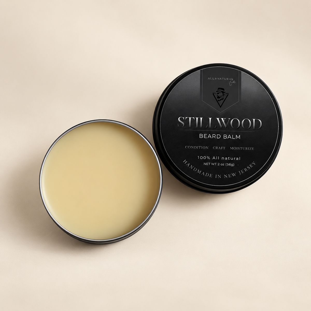 An open round tin of Stillwood Beard Balm showing the pale cream balm inside, next to its black lid on a light beige background.