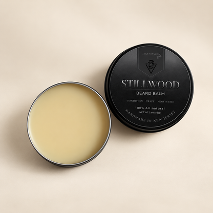 An open round tin of Stillwood Beard Balm showing the pale cream balm inside, next to its black lid on a light beige background.