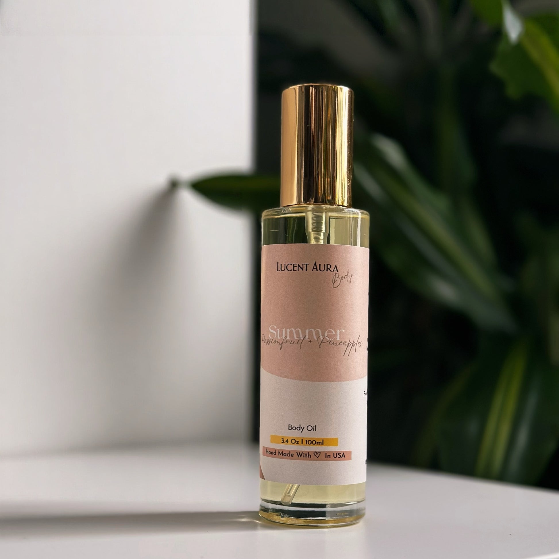 Bottle of Lucent Aura body oil on a white surface with a blurred green plant in the background