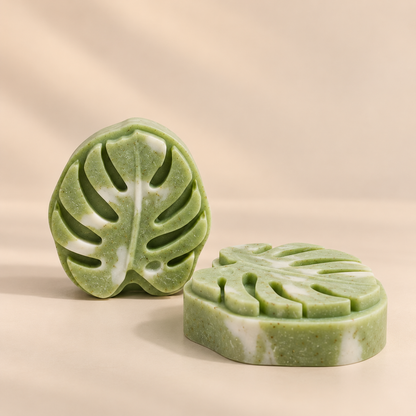 Two green marbled soap bars shaped like monstera leaves, displayed on a warm beige background.