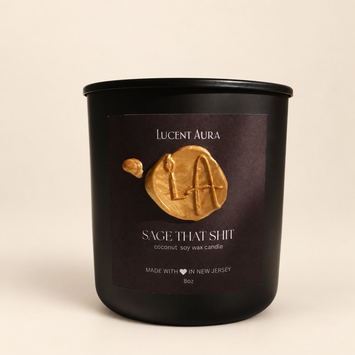 A matte black soy wax candle jar by Lucent Aura with a dark brown label featuring a gold wax seal logo and the scent name 'Sage That Shit'.